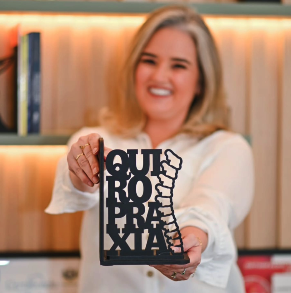 Ludmila B Maia segurando peça decorativa com a palavra quiropraxia